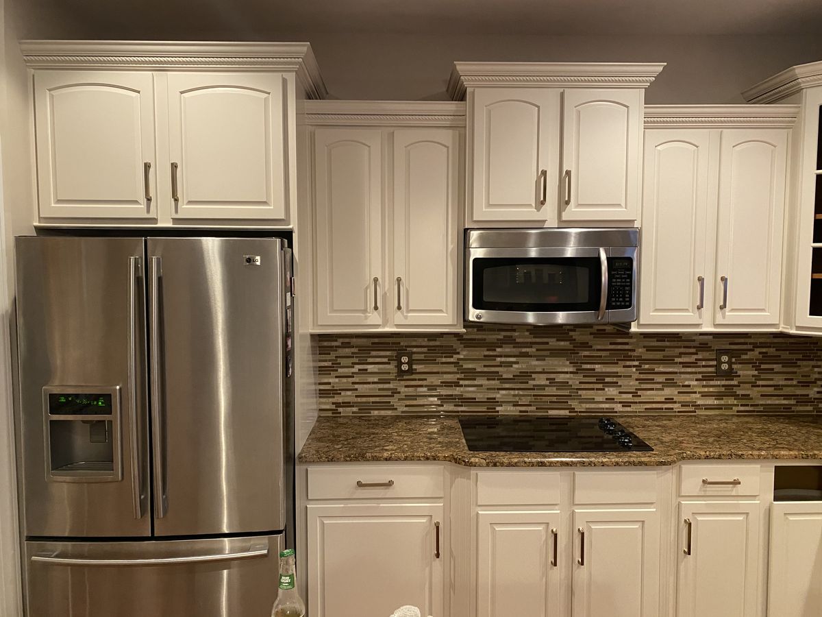 Kitchen with cabinets refinished in a smooth off-white finish with brushed-nickel pulls, above a granite counter, tile backsplash, and stainless appliances.