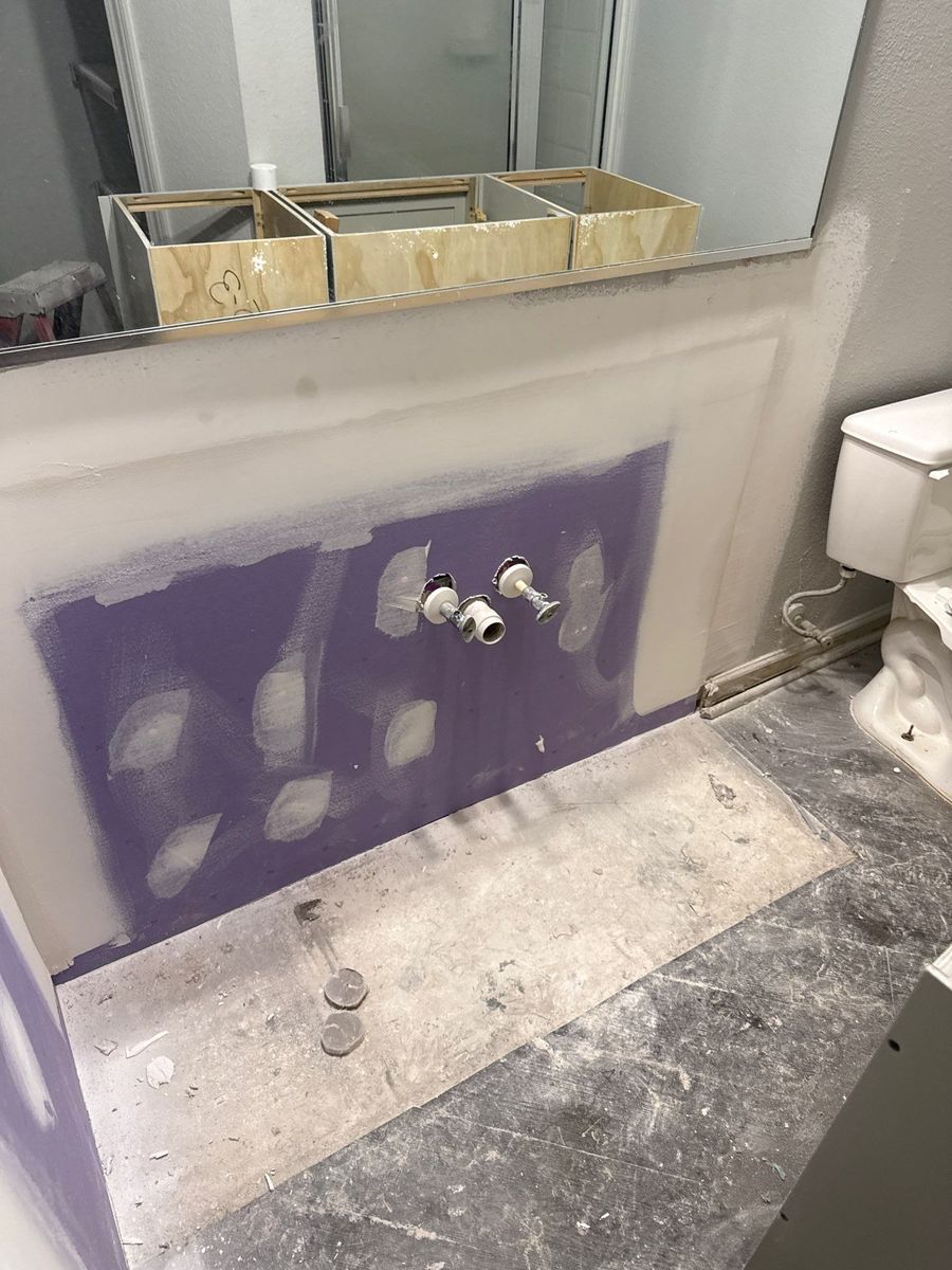 Bathroom wall behind a removed vanity with new moisture-resistant drywall installed, taped and mudded, ready for sanding and paint.